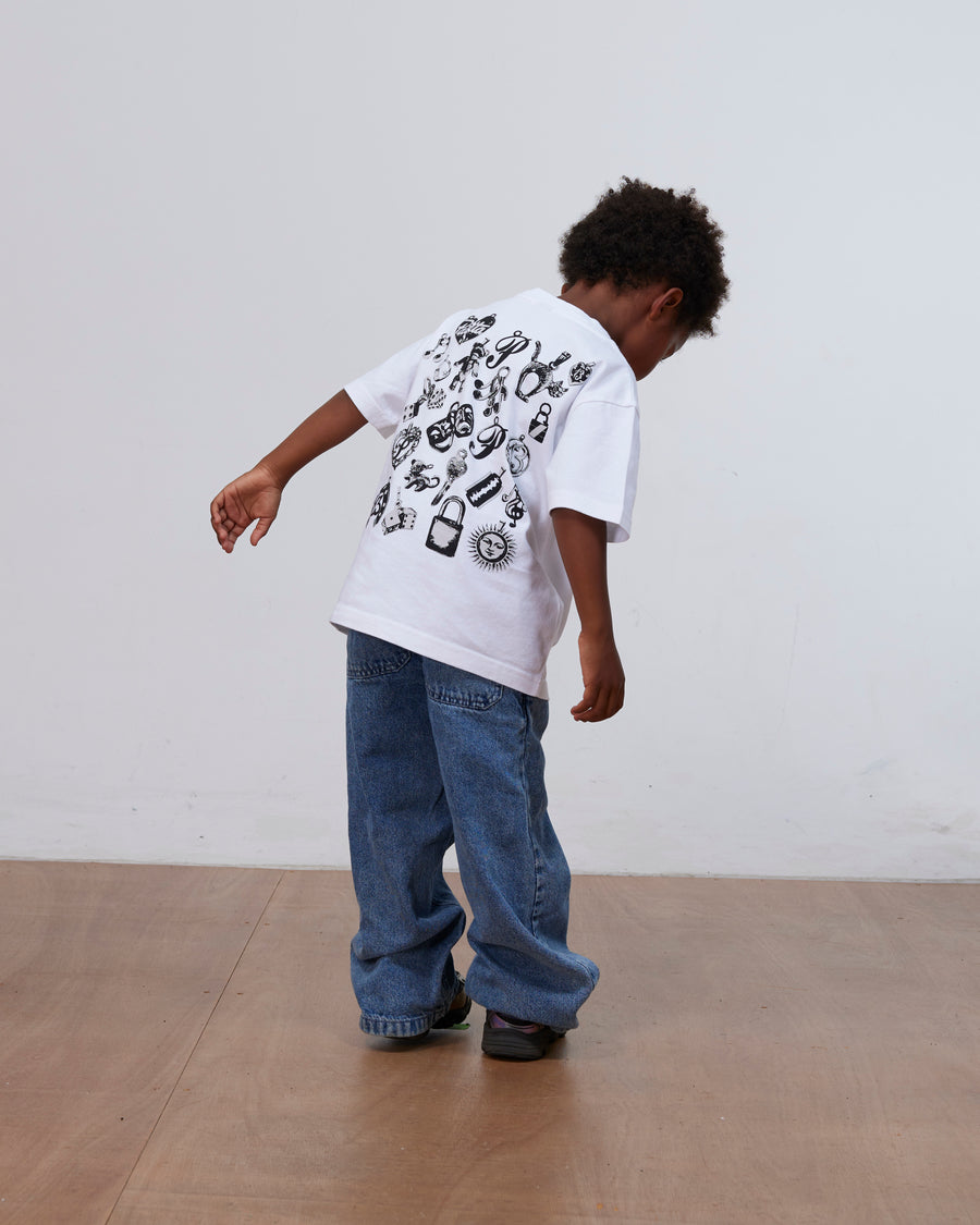 Child wearing the white Patta Kids Charm T-Shirt with back charm graphics and loose denim jeans.
